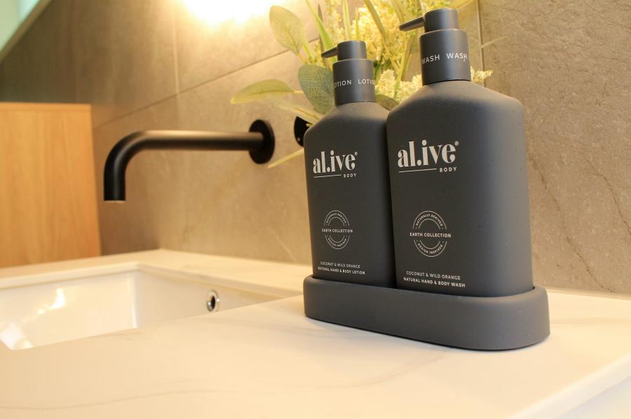 Matte black soap and lotion bottles on a white bathroom basin beside a black wall spout