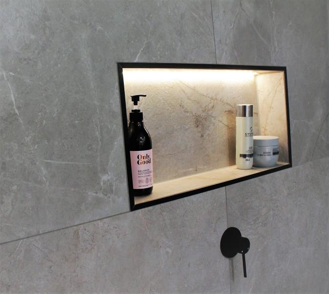 Illuminated recessed shower niche in grey tiled bathroom wall
