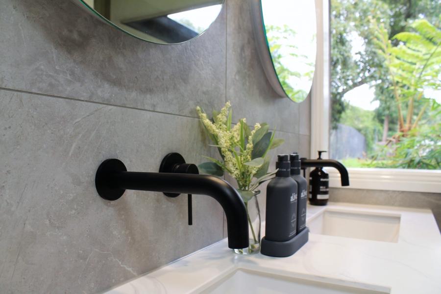 Matte black wall-mounted bathroom tap above a white basin beside a bright window