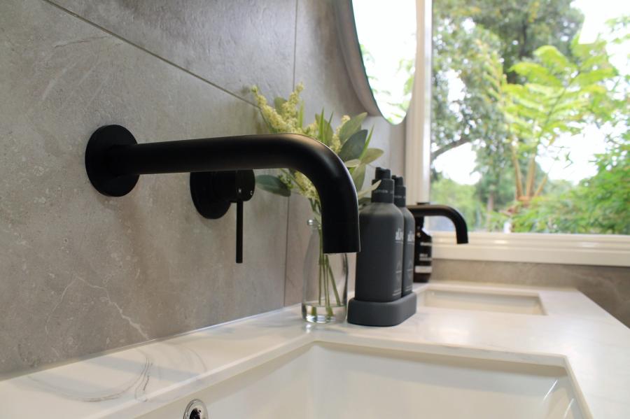 Matte black wall-mounted basin tapware above a white bathroom vanity near a window