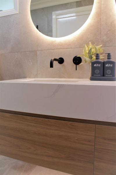 Floating timber vanity with white basin and backlit round mirror in a modern bathroom