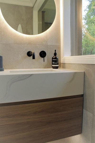 Wall-hung bathroom vanity with round backlit mirror beside a window
