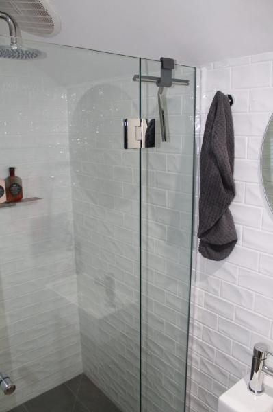 Frameless glass shower with white tiled walls and a dark towel in a modern bathroom
