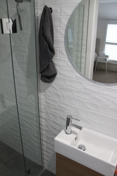 Compact bathroom with glass shower, white subway tiles, round mirror and small wall-hung basin