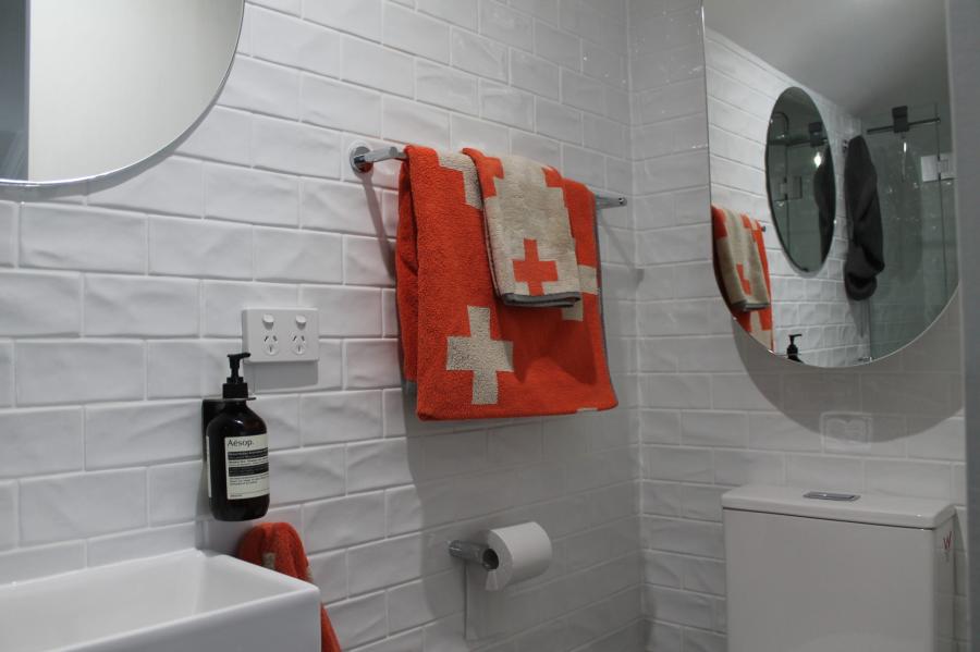 Modern white tiled bathroom wall with round mirror, towel rail and toilet