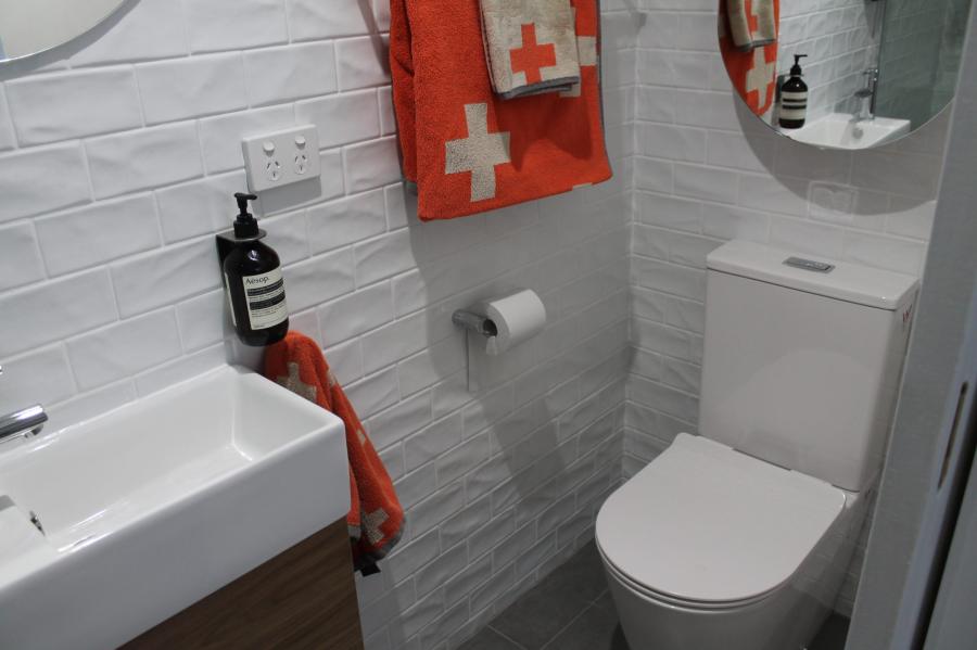 Compact white bathroom with wall-hung vanity, toilet, round mirror and white wall tiles