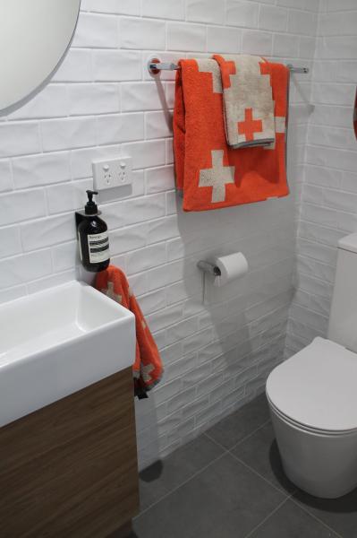 Modern bathroom corner with white vanity, wall-hung toilet and orange towels on white tiled wall