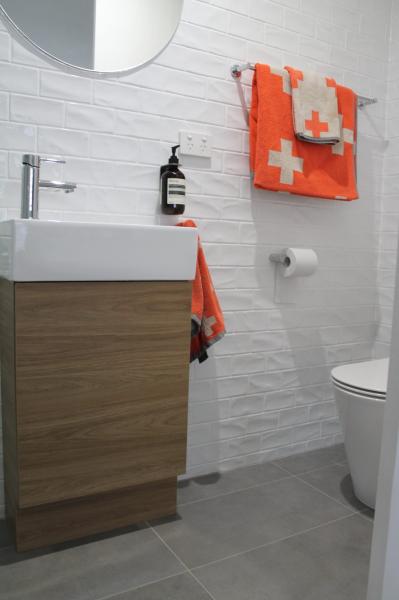 Modern bathroom with timber vanity, white basin, textured tiles and orange towels
