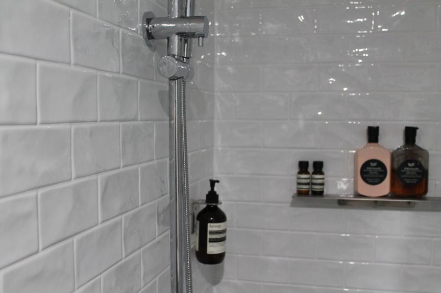 White tiled shower with chrome fixture and recessed shelf holding bathroom products