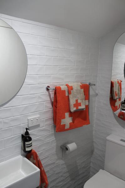 White tiled bathroom wall with round mirror, hand towel, toilet roll and basin