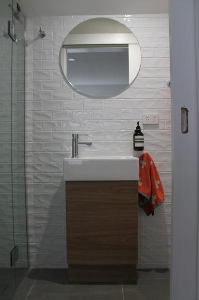 Modern bathroom vanity with round mirror, white tiles and glass shower screen