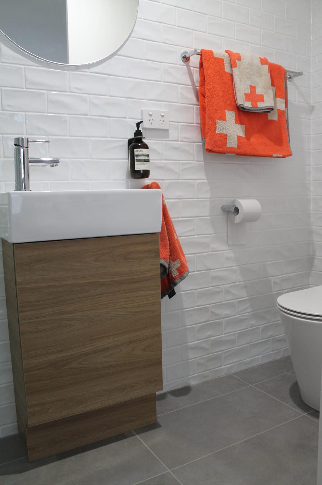 Modern bathroom vanity with white subway tiles and orange towels