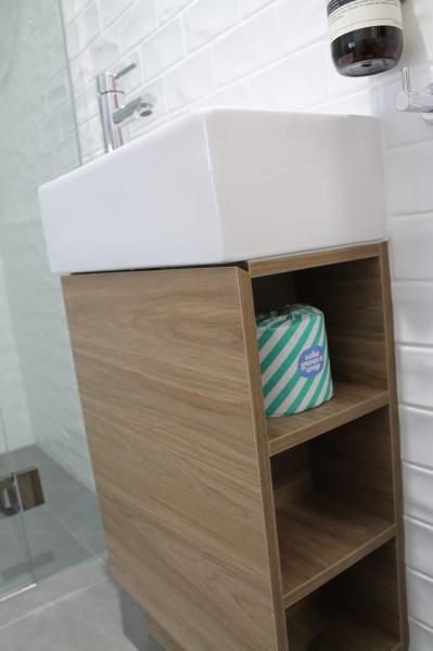 Compact timber-look bathroom vanity with white basin and open shelves beside a glass shower