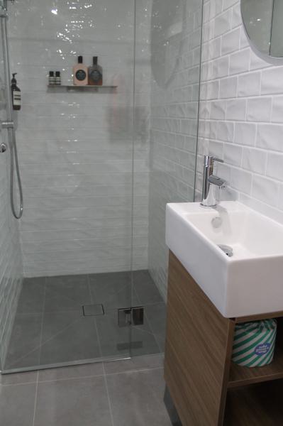 Modern white tiled shower with frameless glass screen and compact timber vanity