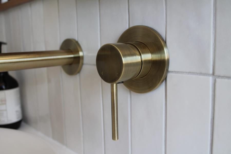 Brushed brass shower mixer and rail on white tiled bathroom wall