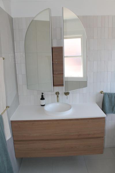 Floating timber vanity with vessel basin and twin arched mirrors in a bright modern bathroom