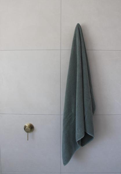 Grey towel hanging on a brass hook against light bathroom wall tiles