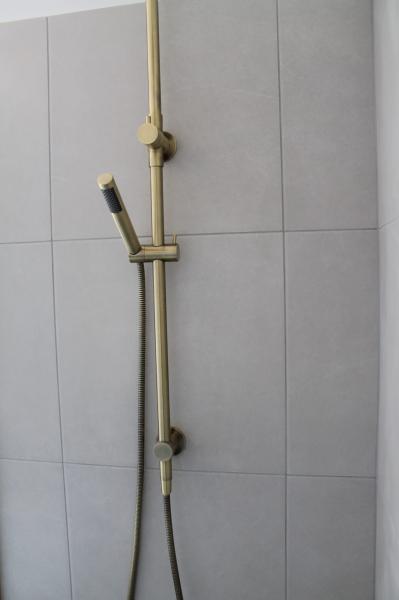 Brushed brass handheld shower on light grey tiled bathroom wall