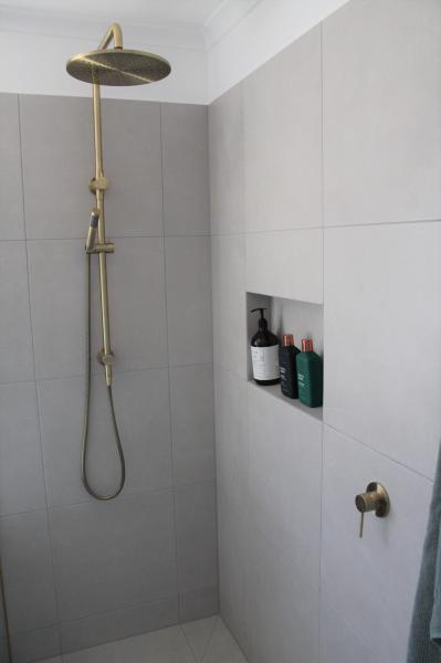 Walk-in shower with brushed brass fixture and recessed niche in grey tiled bathroom