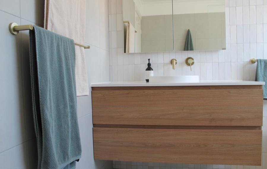 Floating timber vanity with white basin, brass taps and round towel rail in a modern bathroom