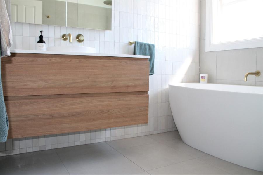Modern bathroom with floating timber vanity and freestanding bath beside a frosted window