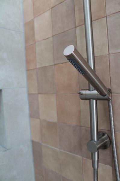 Close-up of a chrome handheld shower on a tiled bathroom wall