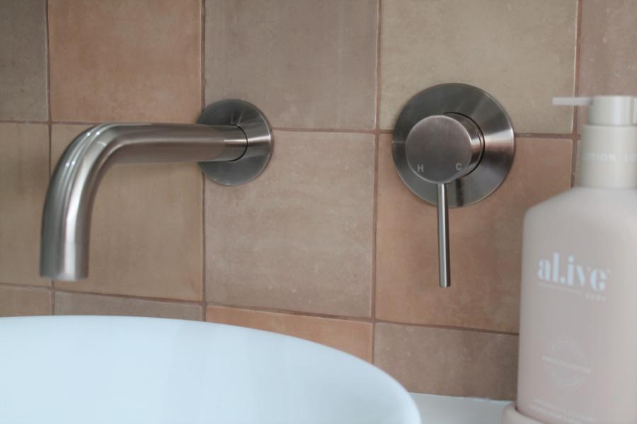 Wall-mounted bathroom tap and mixer above a white basin with beige tiled splashback