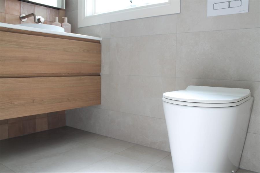 Wall-hung timber vanity beside modern white toilet in a tiled bathroom