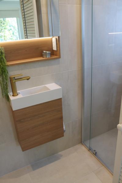 Compact modern bathroom vanity beside a glass shower with timber cabinetry