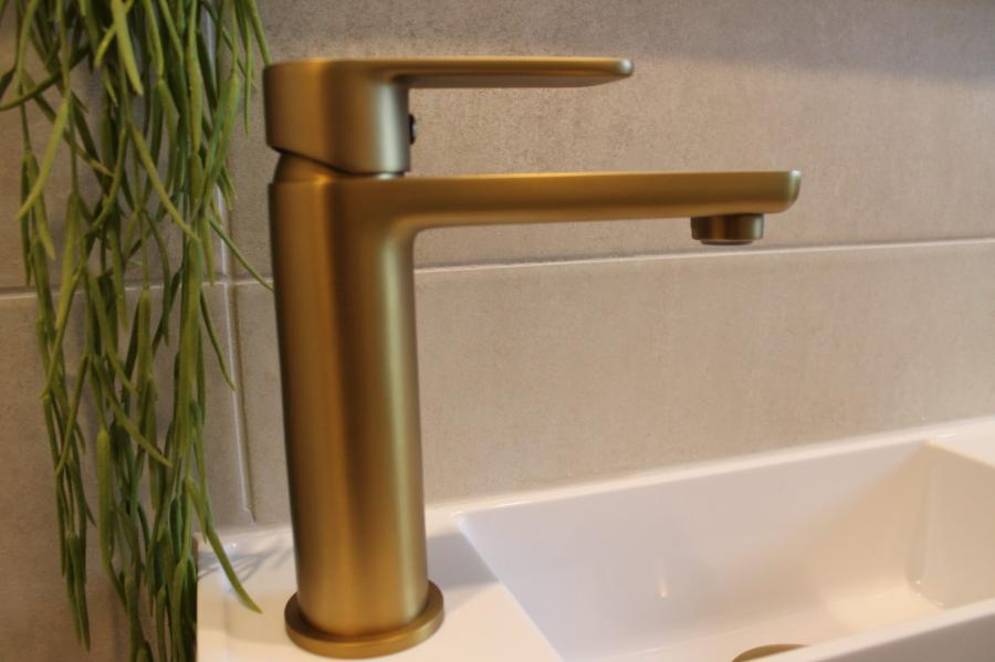 Brushed brass bathroom mixer tap beside a white basin and tiled splashback