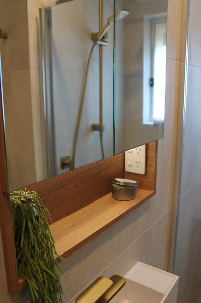 Bathroom mirror cabinet with timber shelf beside a shower in a modern tiled bathroom