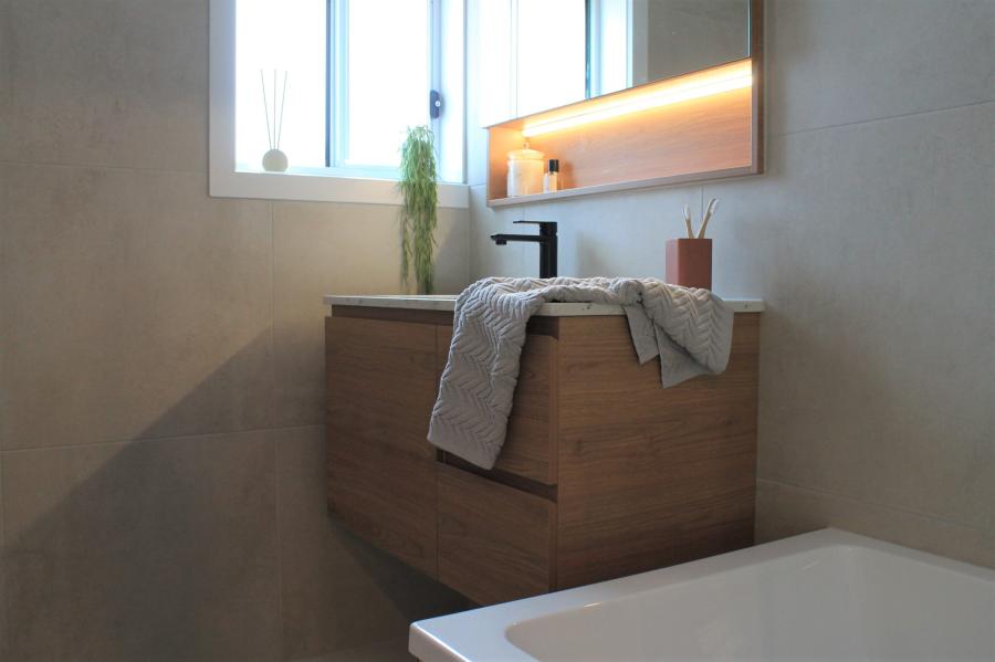 Modern bathroom vanity with basin, mirror lighting and bathtub in a neutral tiled bathroom