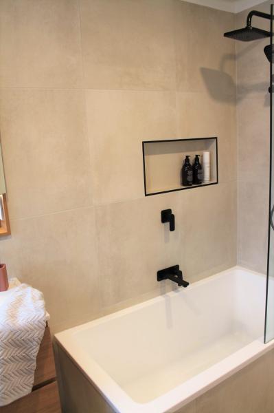 Modern white bathtub with wall niche and black shower fittings in a tiled bathroom