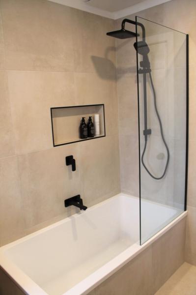 Modern bathtub shower with beige wall tiles, black tapware and recessed niche