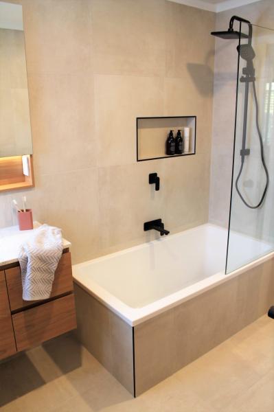 Modern beige tiled bathroom with bathtub, shower screen and recessed niche
