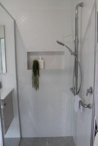 Modern white walk-in shower with recessed niche, handheld shower, and grab rail