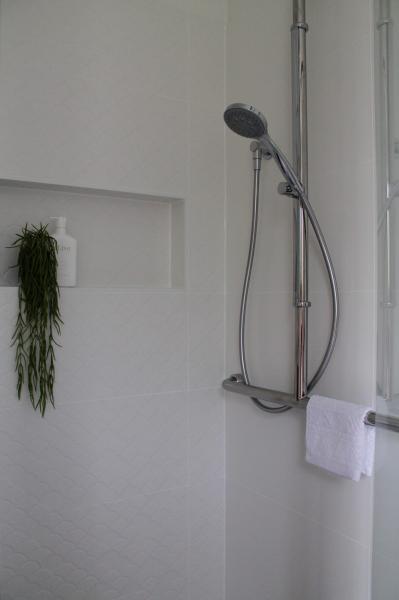 Modern white tiled shower with handheld showerhead, recessed niche and hanging plant