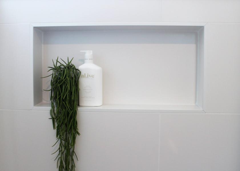 Minimal white tiled shower niche with bottle and trailing plant