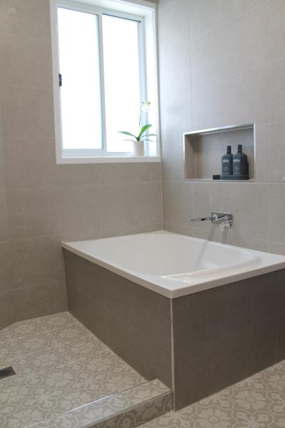 Modern tiled bathroom with built-in bath, window and recessed shelf