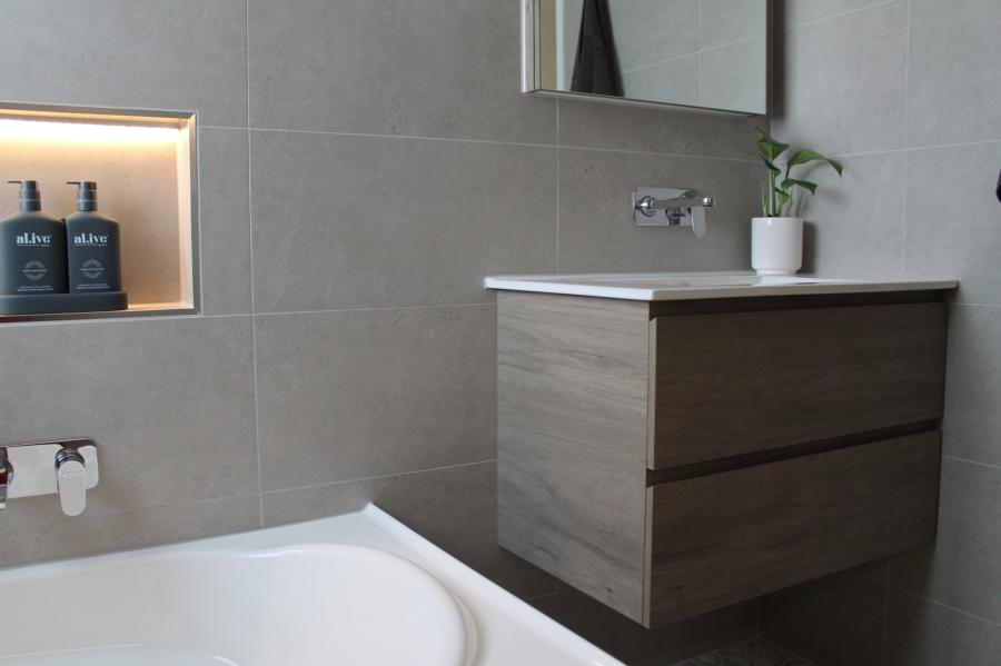 Modern bathroom vanity beside bathtub with recessed niche and grey wall tiles
