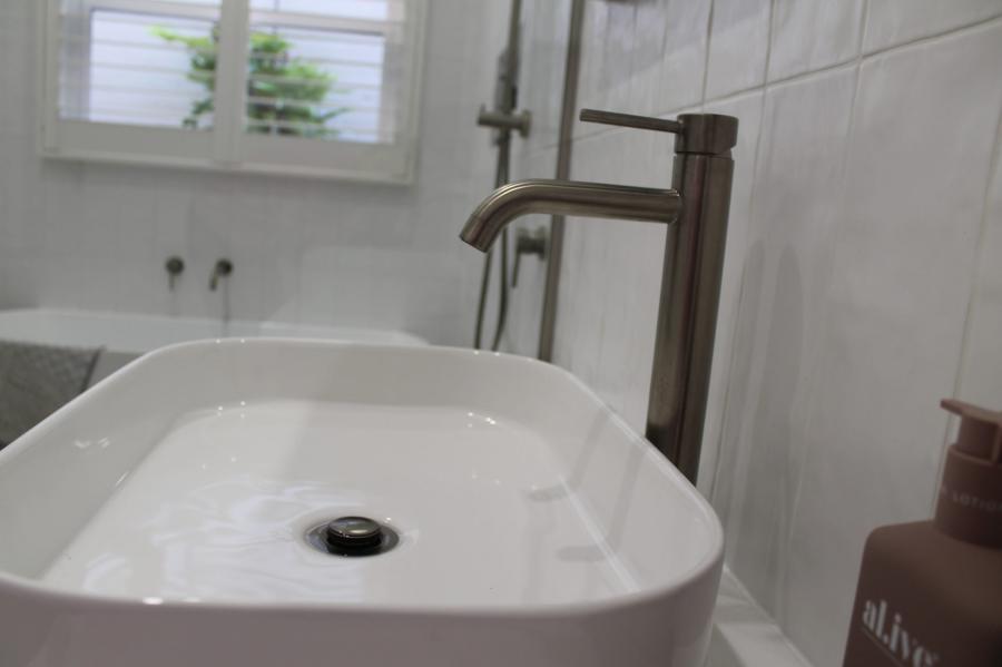 White bathroom basin with brushed tapware in a modern tiled bathroom