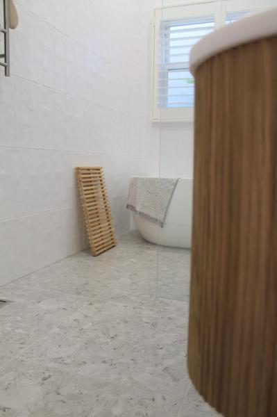 Modern white tiled bathroom floor with timber vanity, toilet and folded towel