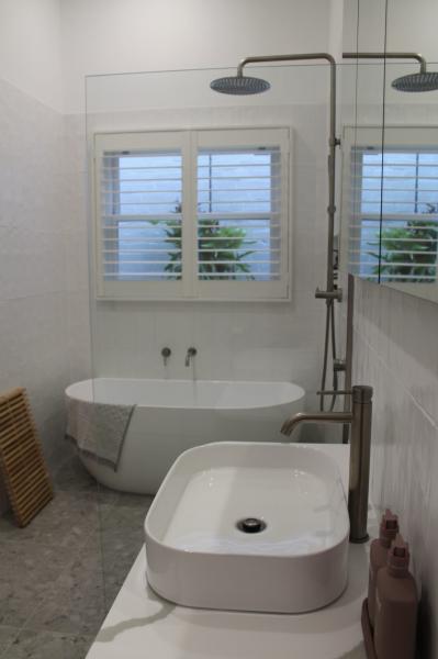 Modern white bathroom with freestanding bath, vessel basin and black shower beside shuttered windows