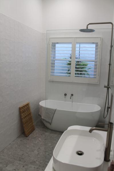 Modern white bathroom with freestanding bath, walk-in shower and louvre window