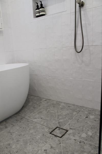 White tiled walk-in shower area with freestanding bath and floor waste