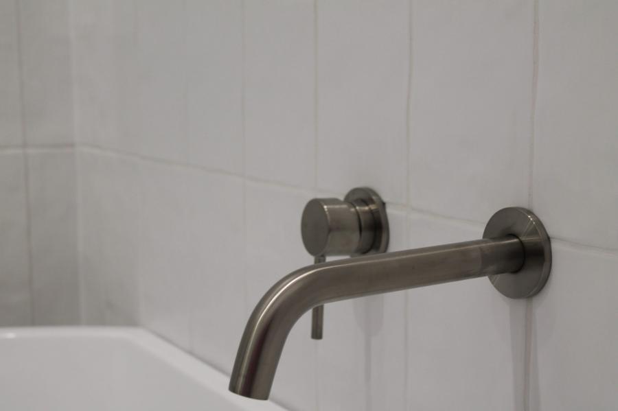 Wall-mounted chrome bath spout on white tiled bathroom wall