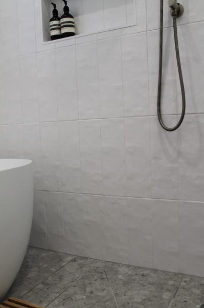 White tiled shower area with niche shelving, freestanding bath edge and handheld shower