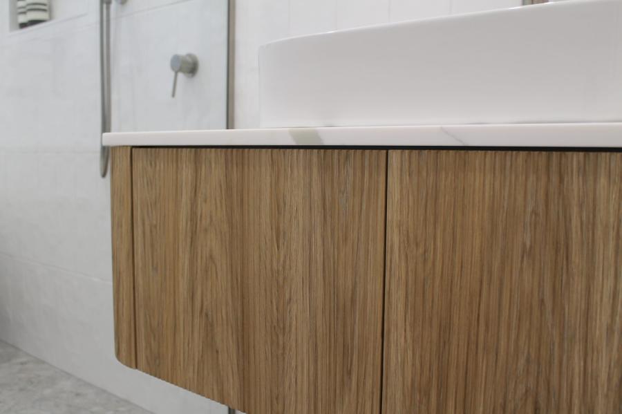 Floating timber bathroom vanity beneath a white basin beside a frameless shower