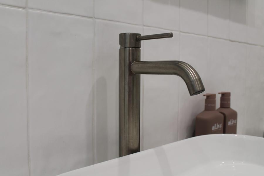 Brushed metal bathroom basin tap beside a white basin and wall tiles