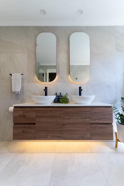 Modern double vanity bathroom with oval mirrors, vessel basins and warm under-cabinet lighting